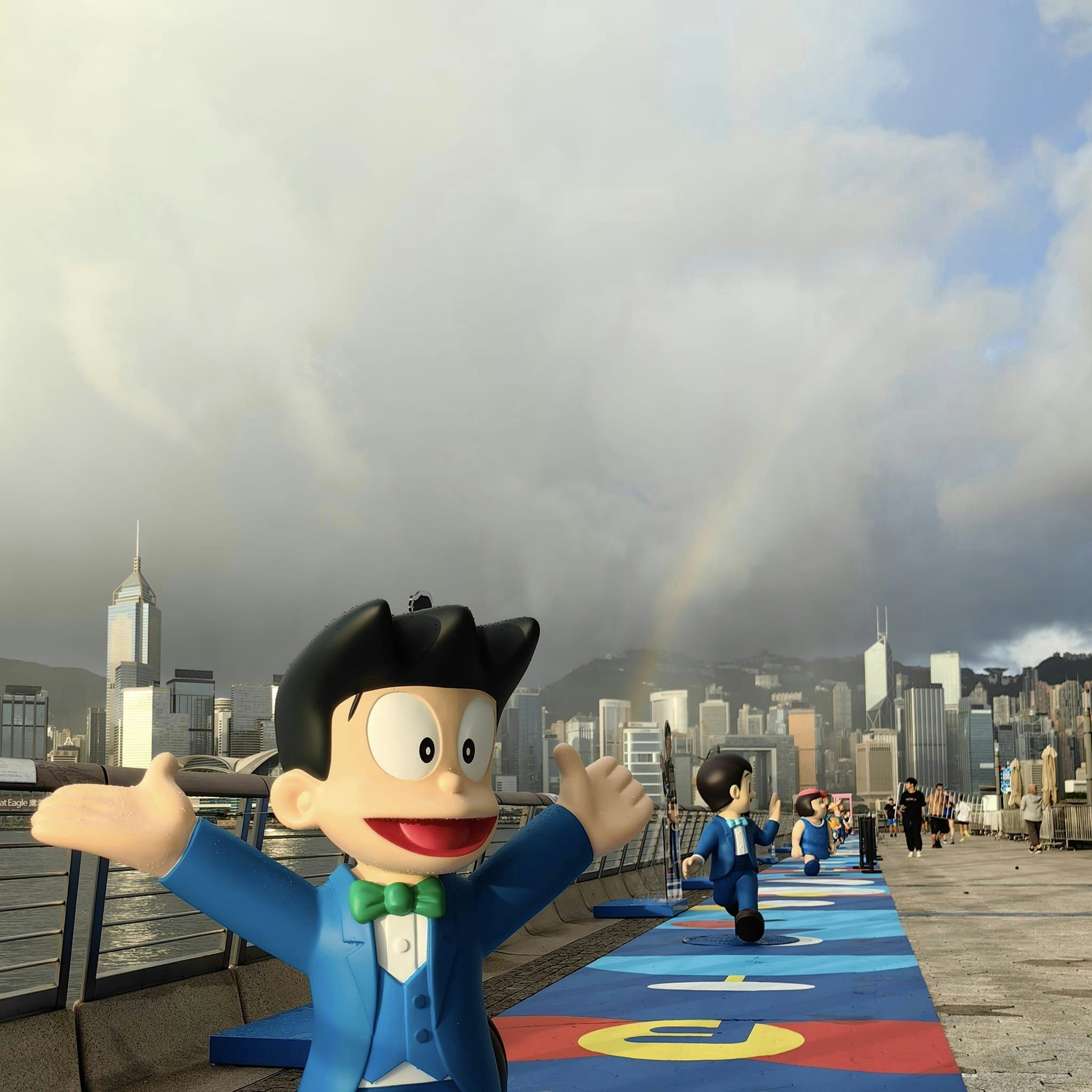 7月12日早上下了一場驟雨，維港出現彩虹，有市民拍攝以《100%多啦A夢& FRIENDS》巡迴特展香港站為景象的情景。圖為06:30攝於星光大道。（Peter Lai攝／Facebook專頁社區天氣觀測計劃 CWOS圖片)
