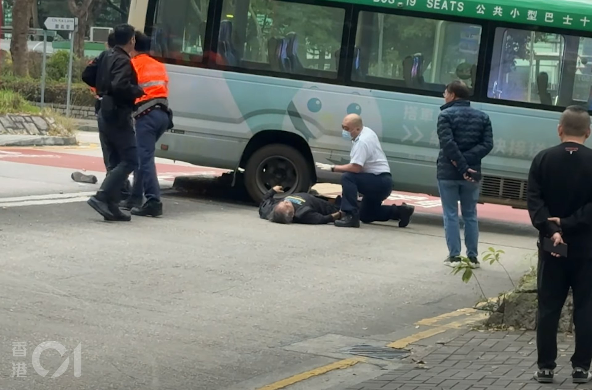 涉事小巴司機倒臥車底旁,一隻鞋飛脫;有救護員上前施援。(讀者提供影片截圖) 涉事小巴司機倒臥車底旁,一隻鞋飛脫;有救護員上前施援。(讀者提供影片截圖)