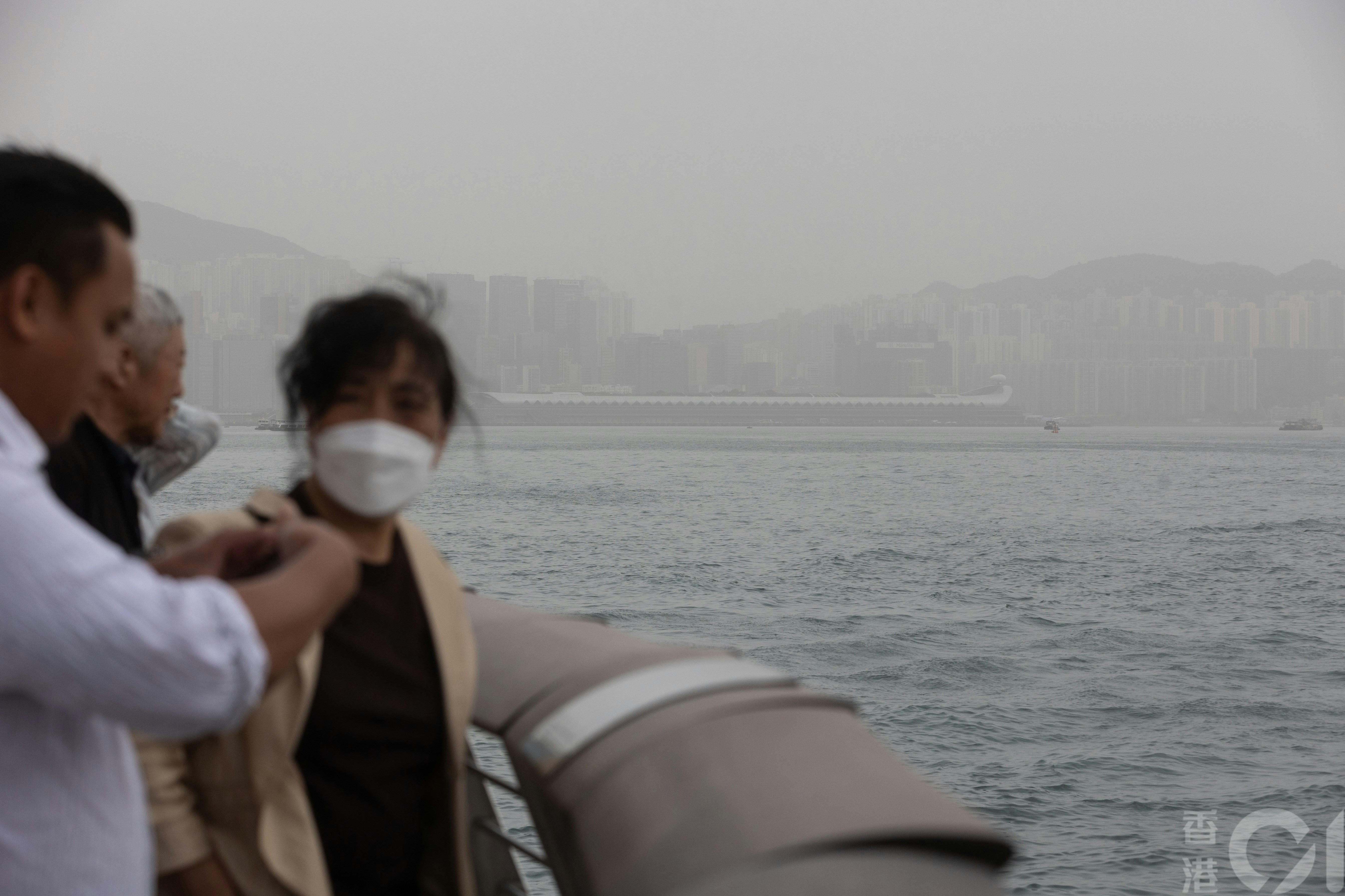 本港4月13日受沙塵天氣影響，維港一片朦朧，到尖沙咀海旁的市民及遊客，不少人戴了口罩。（廖雁雄攝）