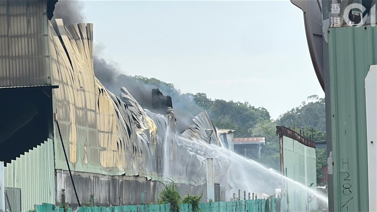 消防員持續向火場射水，濃煙不斷冒上半空，現場不時傳出巨響，相信是貨倉內支架墮下所致，貨倉頂部鐵皮已經倒塌，周邊鐵皮彎曲。（黃煦緻攝）