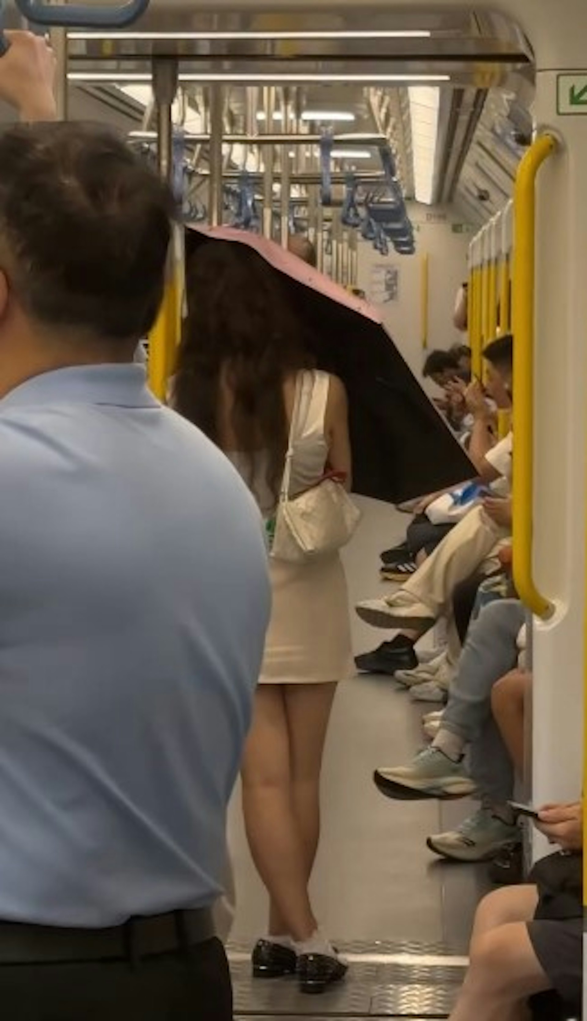 1名長頭髮、身穿無袖連身裙的女乘客搭乘港鐵時,於車廂內打開縮骨遮,擋着自己正前方。(threads影片截圖)