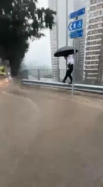 穿西裝、着皮鞋男子，撐着雨傘以「走鋼線」方式沿護欄前行，步步為營，只為走過被激流「封鎖」的道路上班。（Threads＠steve66666）