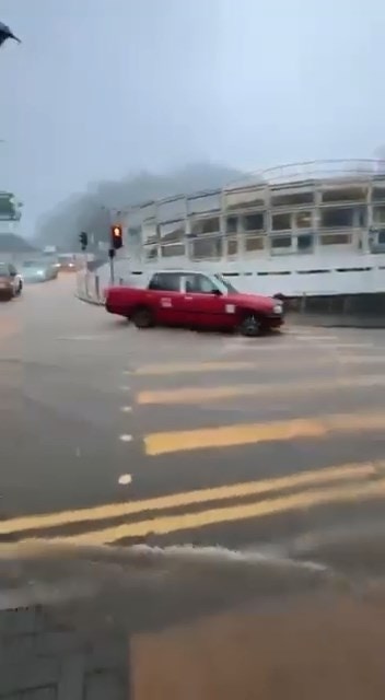 穿西裝、着皮鞋男子，撐着雨傘以「走鋼線」方式沿護欄前行，步步為營，只為走過被激流「封鎖」的道路上班。（Threads＠steve66666）