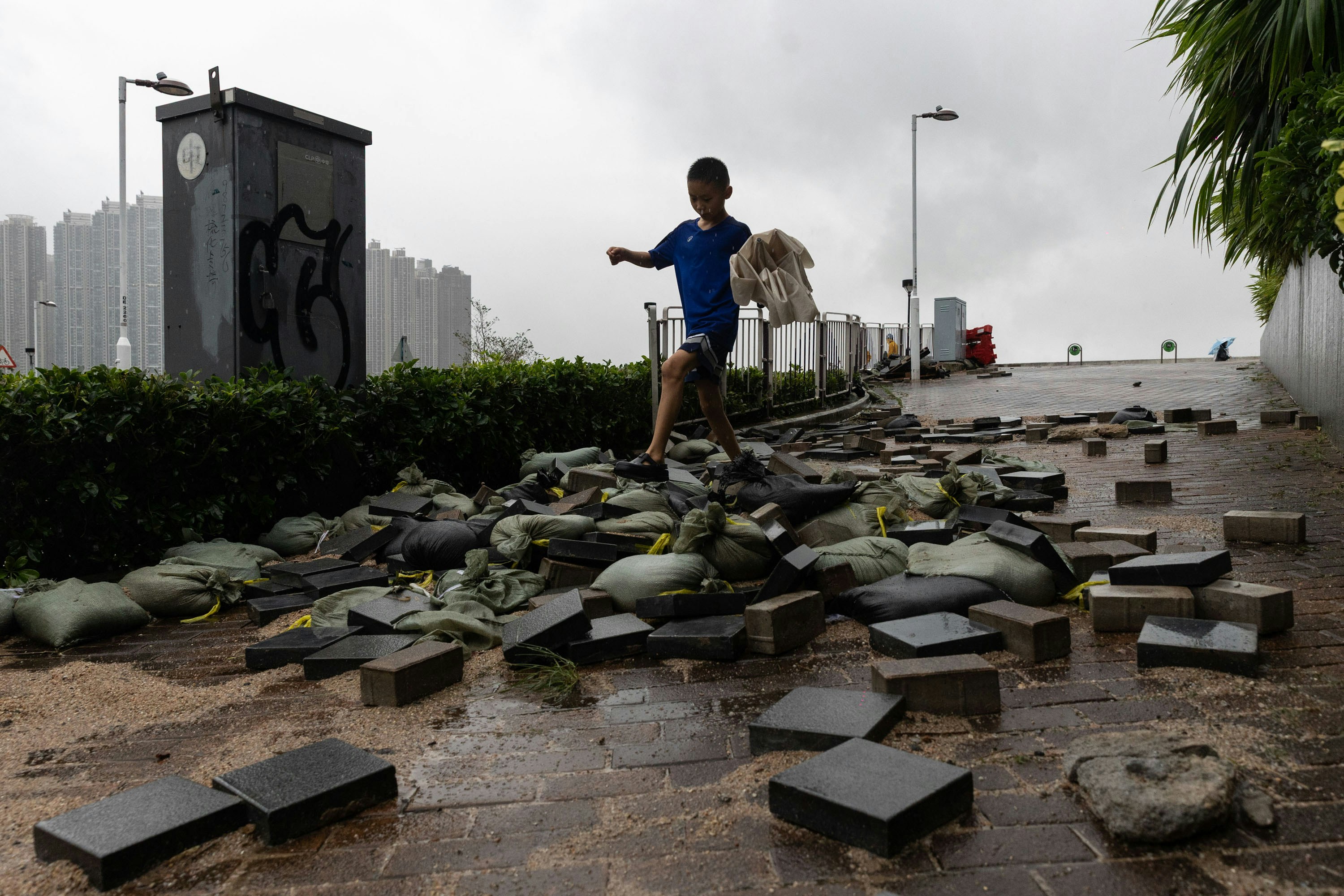 超强台风桦加沙袭港，天文台发出十号飓风信号期间，将军澳涌起大浪，越过海滨。图为受破坏后情况，有小孩走过防洪沙包。（廖雁雄摄）