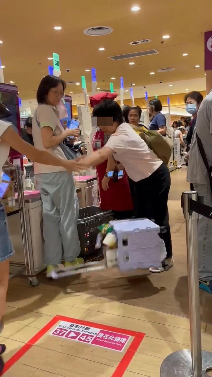 穿粉色上衣的鄉音大媽目露兇光,把港女的「買餸車」一手抬高,再翻倒掉在地上,令內裏貨物散落一地。(網絡影片截圖)