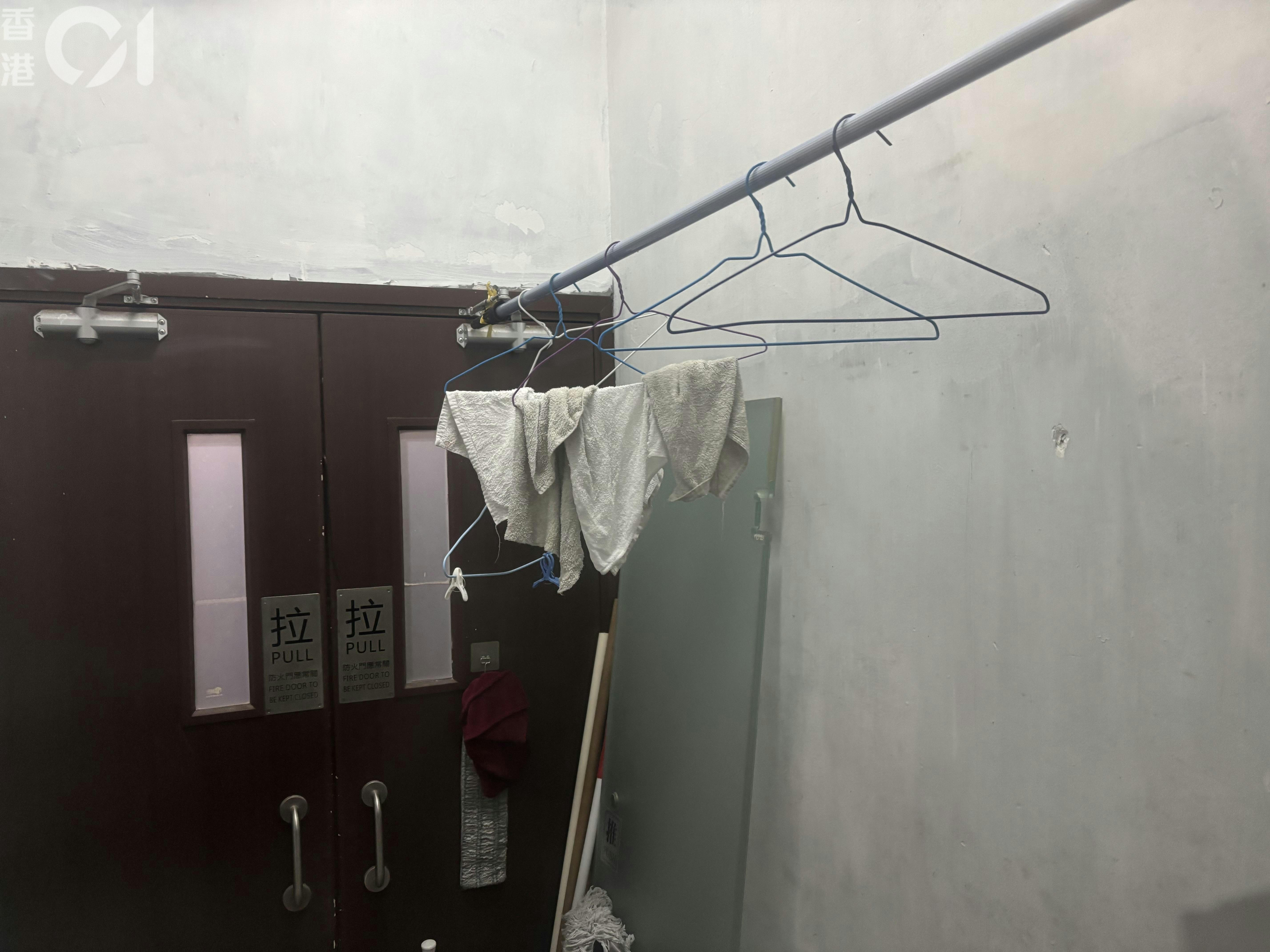 創興廣場13樓mYSTEPS健身中心兩對防火門中間的防煙間的高處架起一條長桿，上面有多個衣架掛起毛巾。防煙間內還有雜物如掃把、膠桶和一隻門。（董素琛攝）