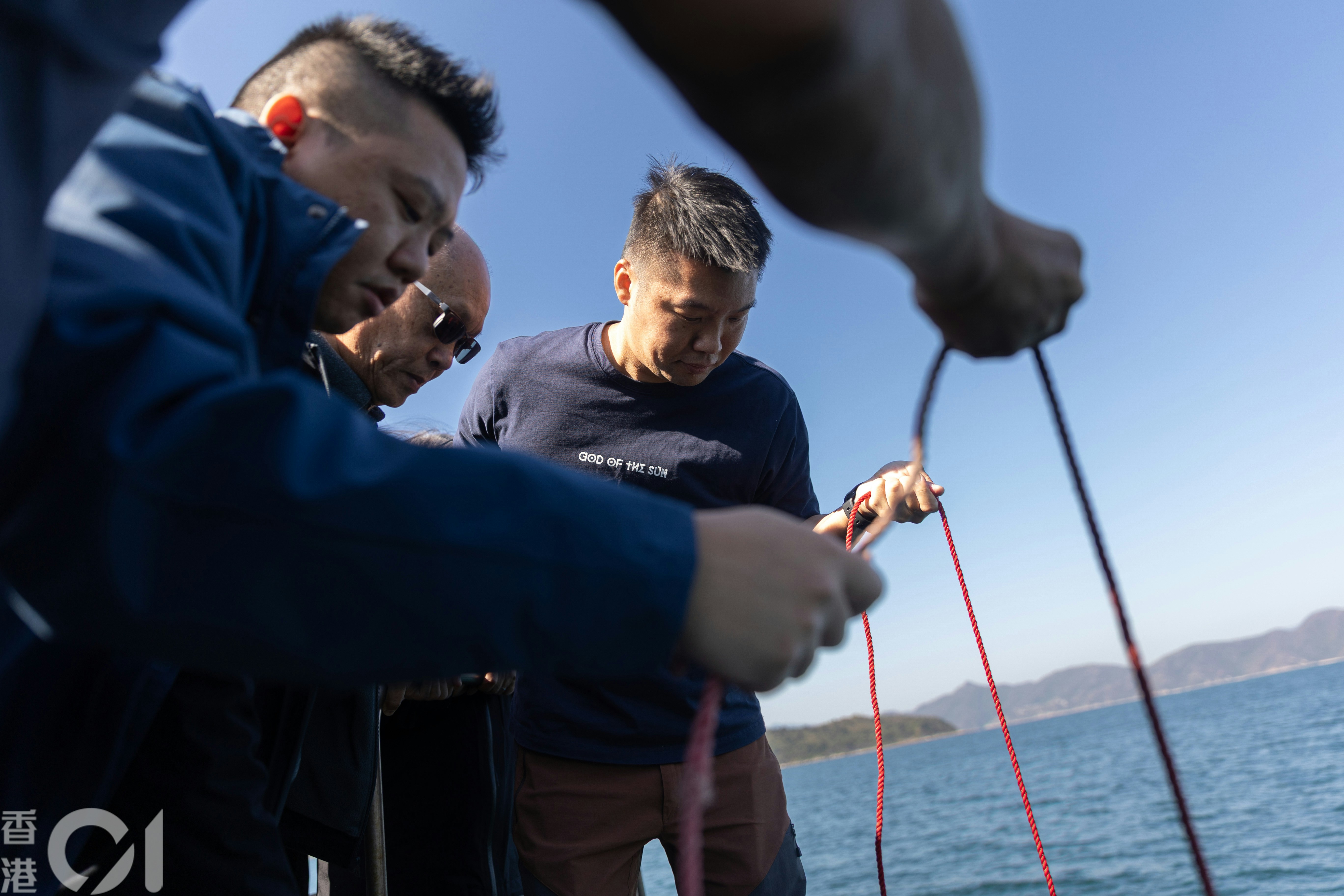 葉先生與兒子阿賢及阿霆持繩將擺放骨灰的膠椅緩緩放進海面。（廖雁雄攝）