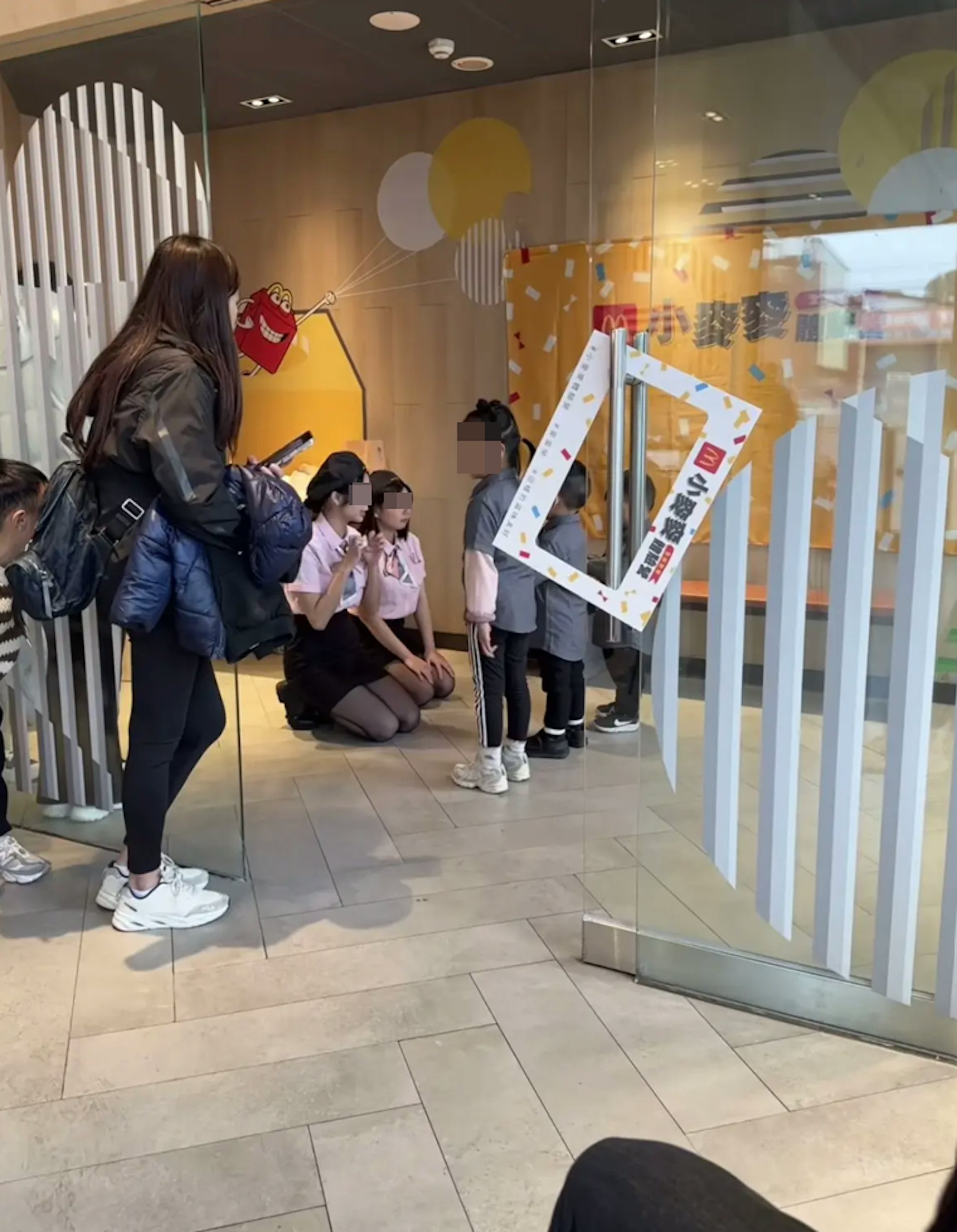 這2名麥當勞女員工皮膚白皙,相當年輕。她們穿上粉衣短袖上制服、黑色短裙、黑色絲襪,並戴上黑色帽,跪在地上向小朋友們講解事情。(影片截圖)
