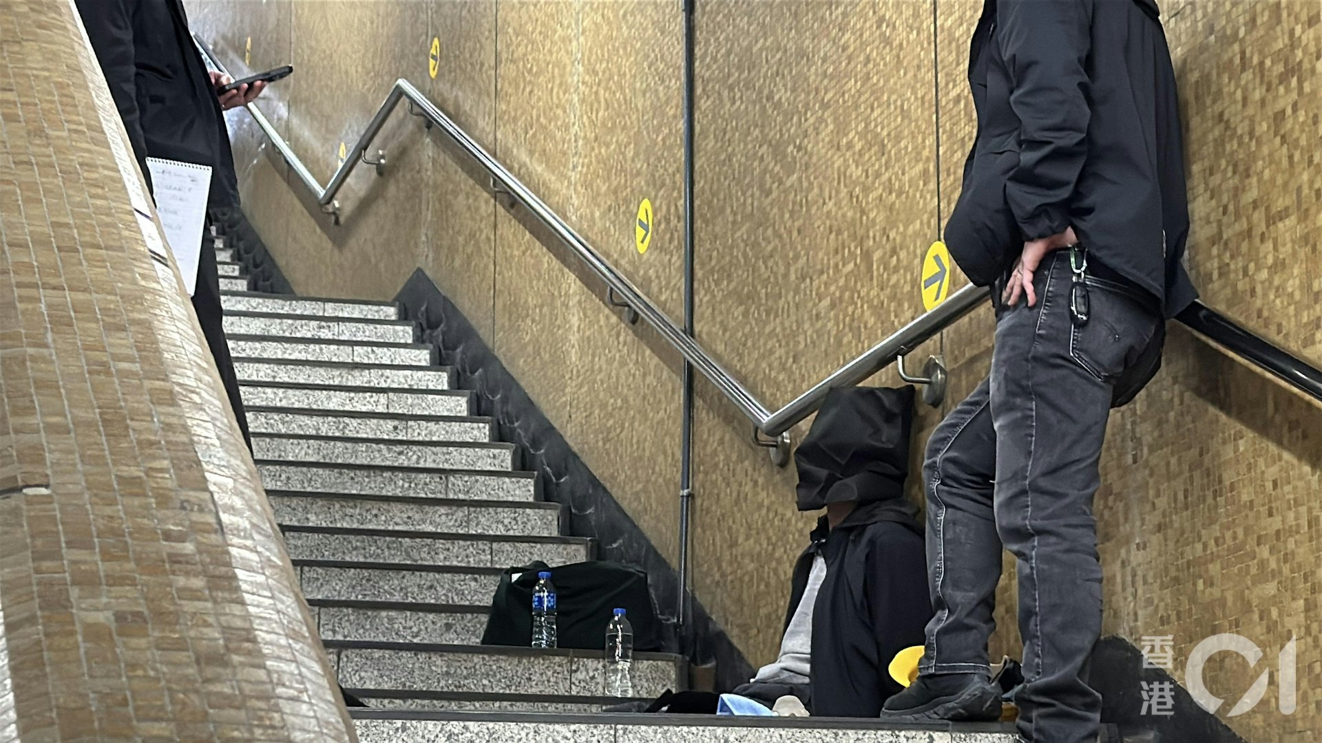 警方在站內拘捕2人,他蒙黑色頭套坐在上環地鐵站B出口的樓梯。(翁鈺輝攝)