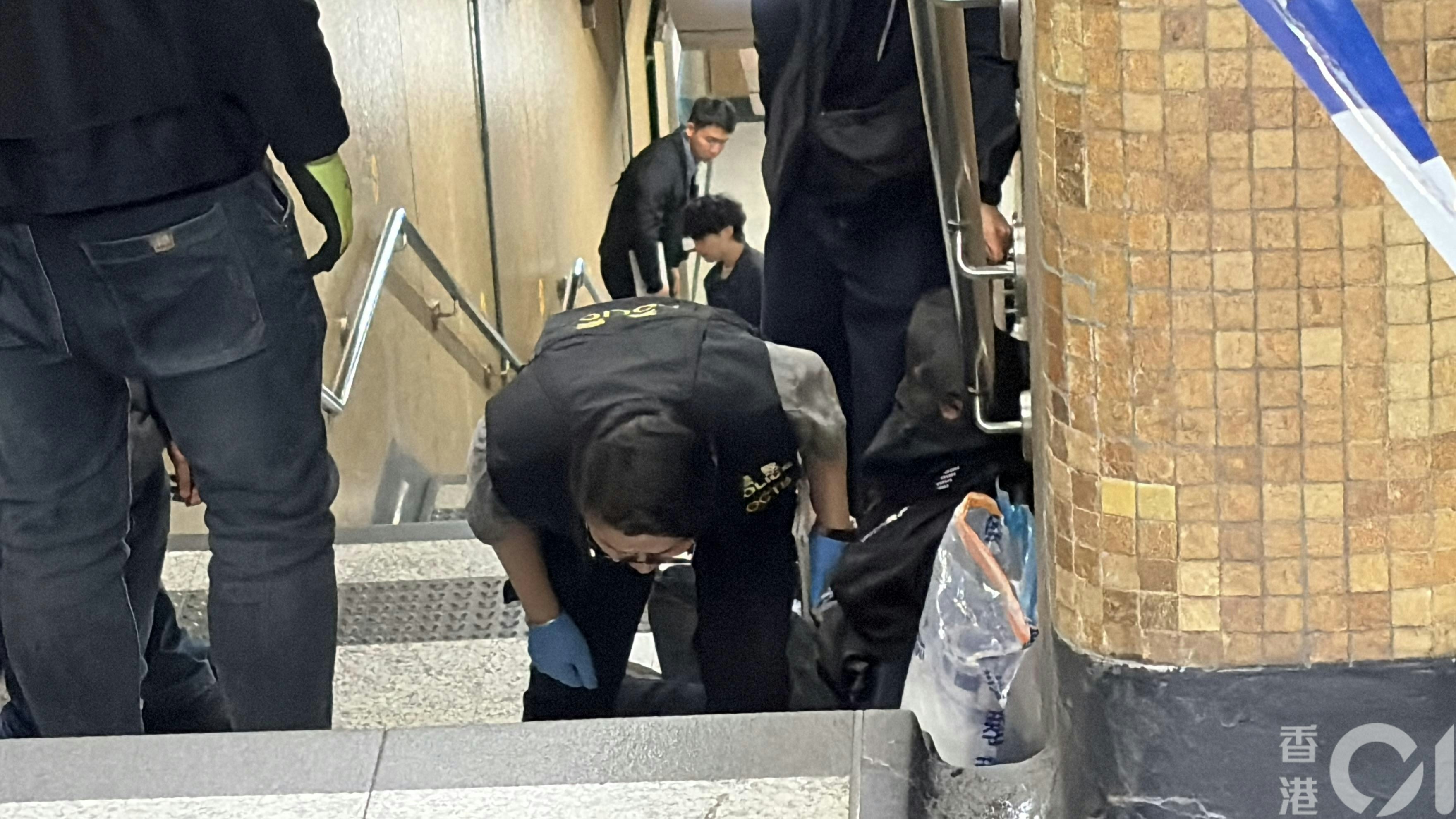 被捕人蒙黑色頭套一左一右坐在上環地鐵站B出口樓梯，被多名警員看守。（黃煦緻攝）