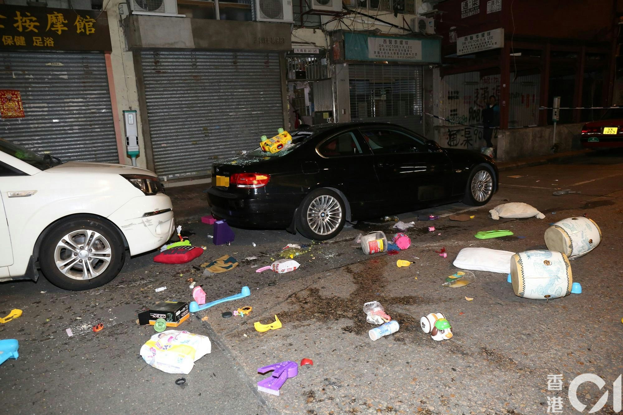 大批雜物從單位窗邊墮下，擊穿樓下私家車車尾車窗，仍然懸掛一個黃色玩具車，馬路散落大量玩具和家居用品，例如枕頭和尿片。（陳永武攝）