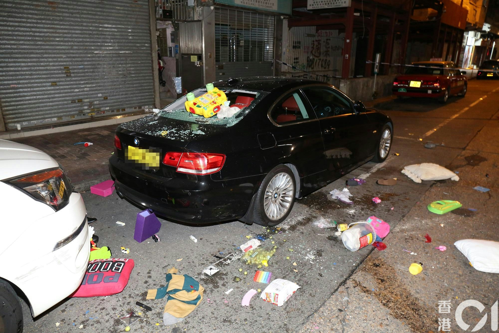 大批雜物從單位窗邊墮下，擊穿樓下私家車車尾車窗，仍然懸掛一個黃色玩具車，馬路散落大量玩具和家居用品，例如枕頭和尿片。（陳永武攝）