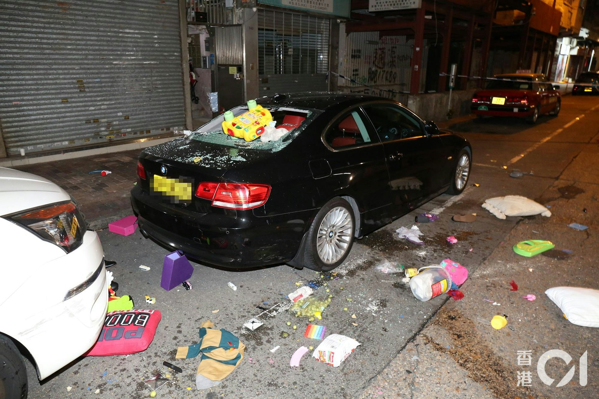大批雜物從單位窗邊墮下,擊穿樓下私家車車尾車窗,仍然懸掛一個黃色玩具車,馬路散落大量玩具和家居用品,例如枕頭和尿片。(陳永武攝)