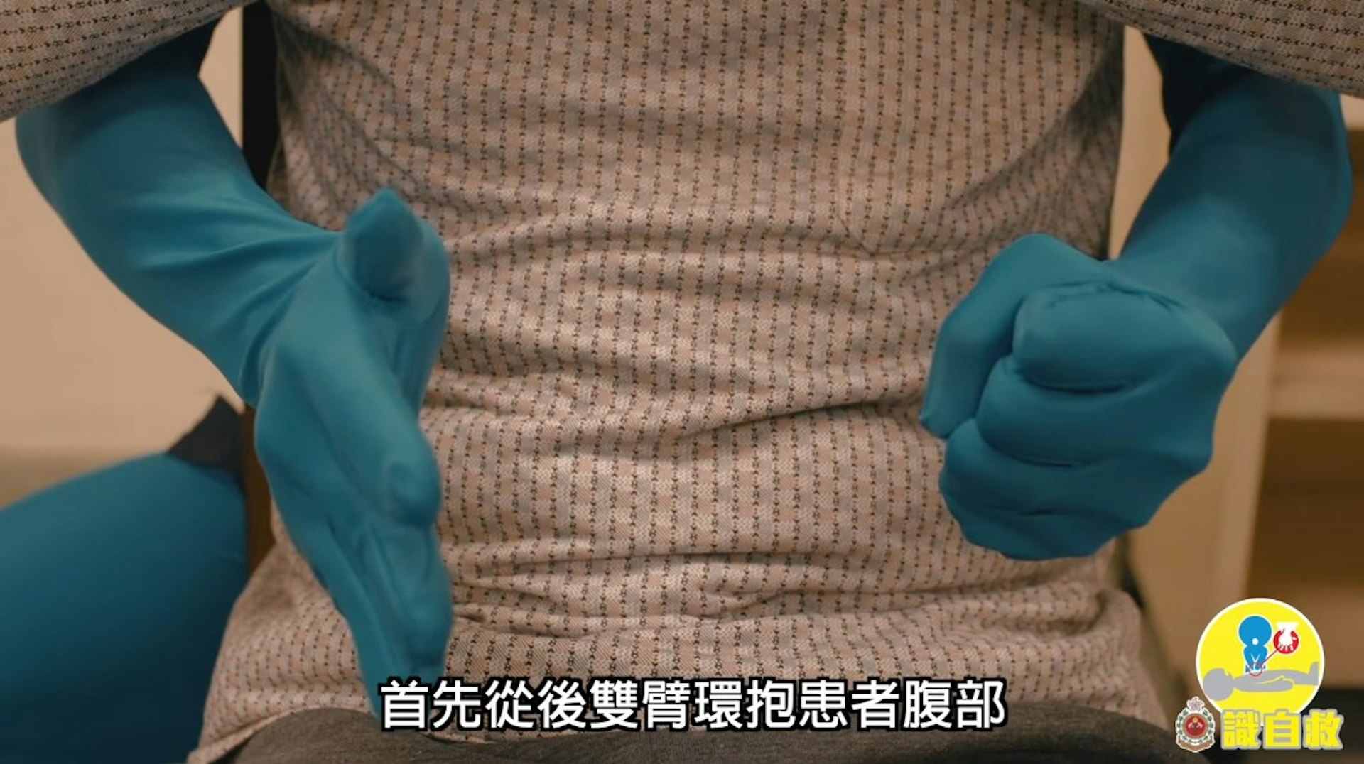 鯁喉患者「謙烈治法」急救步驟1:從後用雙臂環抱患者腰部(消防處YouTube片段截圖)