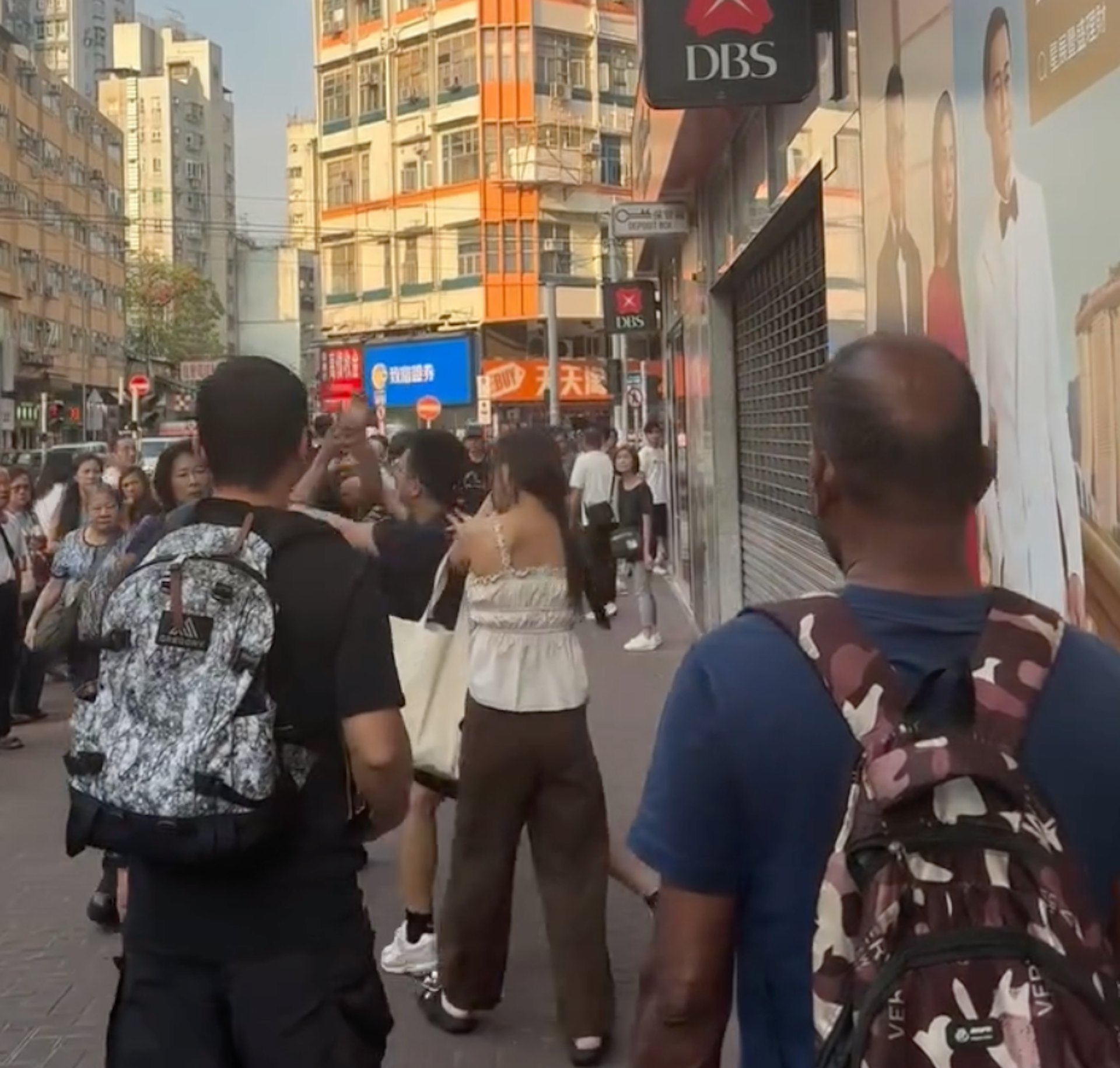背心女右方的眼鏡男揮拳攻擊灰褲男。