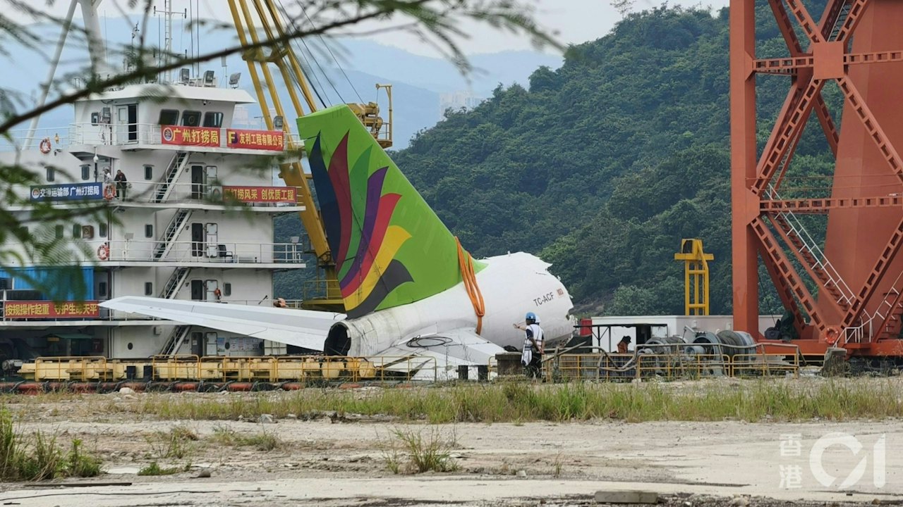 展示飛機殘骸(機尾部分)打撈或搬運現場,具新聞事實證據價值,並可見機身編號及打撈船橫額文字。(78/100) 展示飛機殘骸(機尾部分)打撈或搬運現場,具新聞事實證據價值,並可見機身編號及打撈船橫額文字。