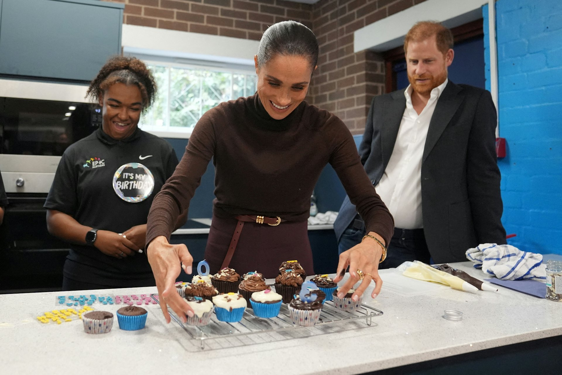 2026年10月15日,英国诺丁汉,哈里王子(Prince Harry,右)与夫人梅根(Meghan Markle,中)访问慈善机构Epic Partners期间准备生日纸杯蛋糕。