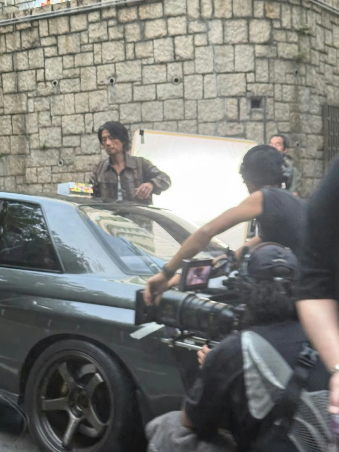 映画の撮影中、暗色の車のそばに立つ黄子華と撮影クルー