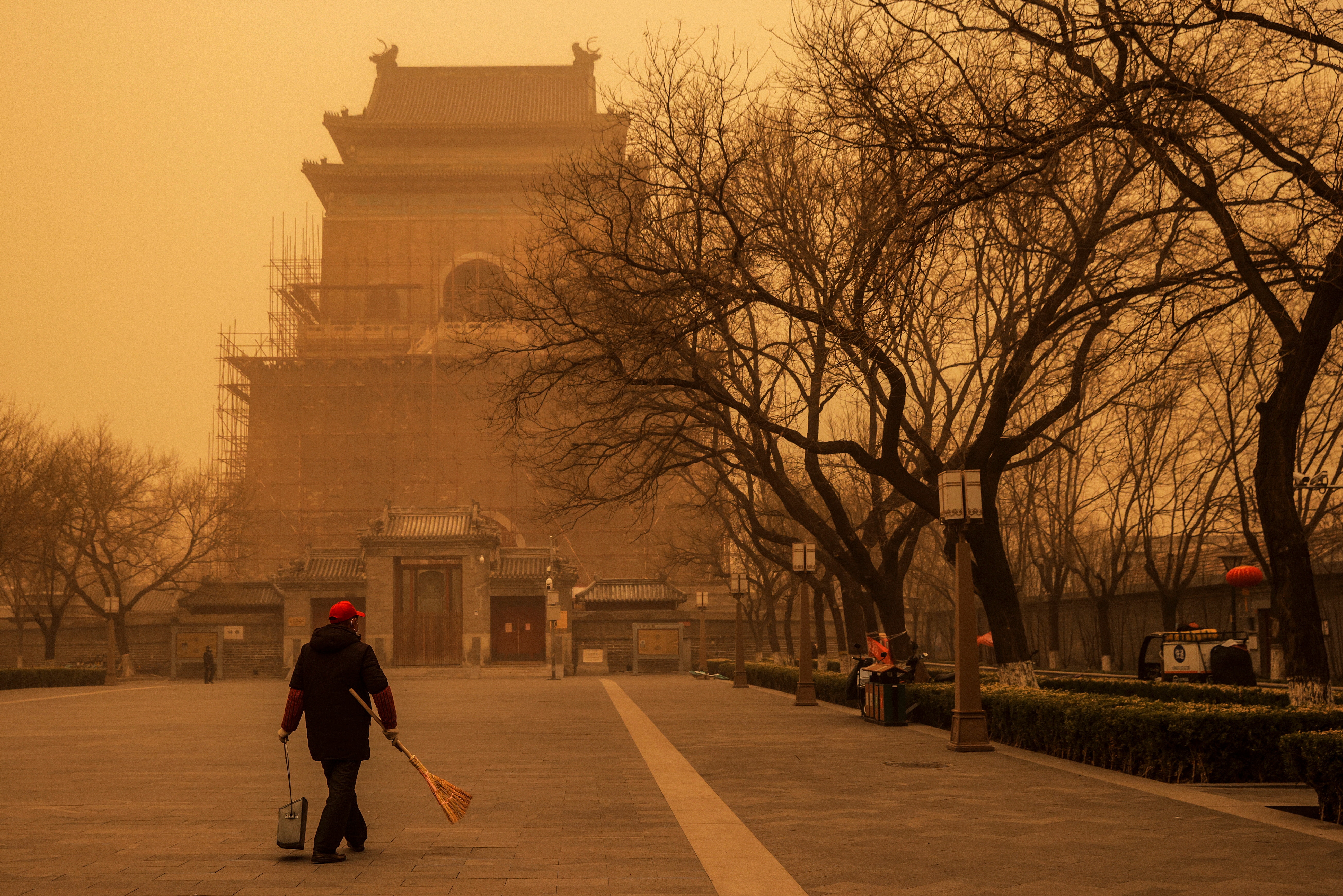 2021年3月15日，当中国北京遭遇沙尘暴时，一个人拿着扫帚和簸箕在早高峰时间行走。路透社/托马斯·彼得A person walks with a broom and dustpan during morning rush hour as Beijing, China, is hit by a sandstorm, March 15, 2021. REUTERS/Thomas Peter